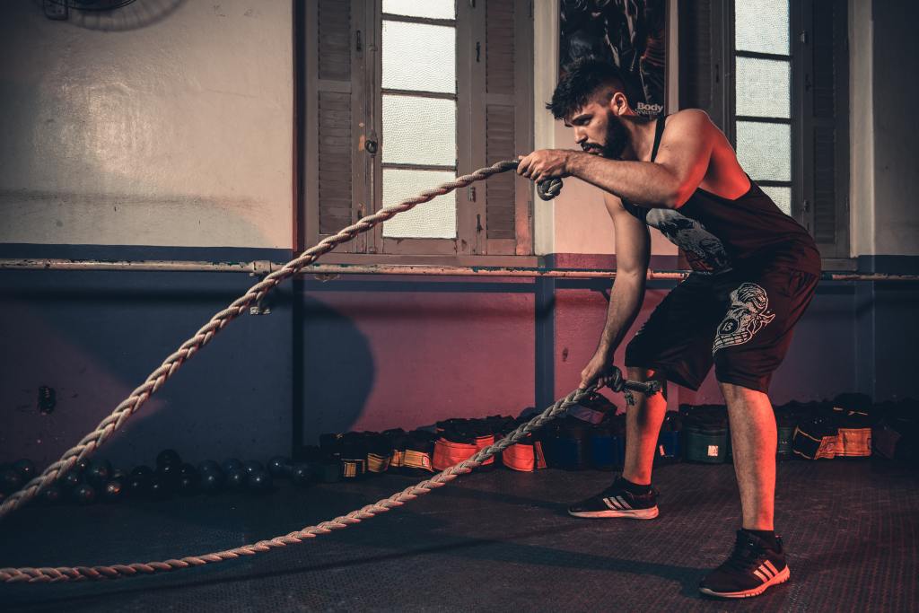  A man in athletic attire performing a rope exercise on the floor, demonstrating physical fitness and strength training