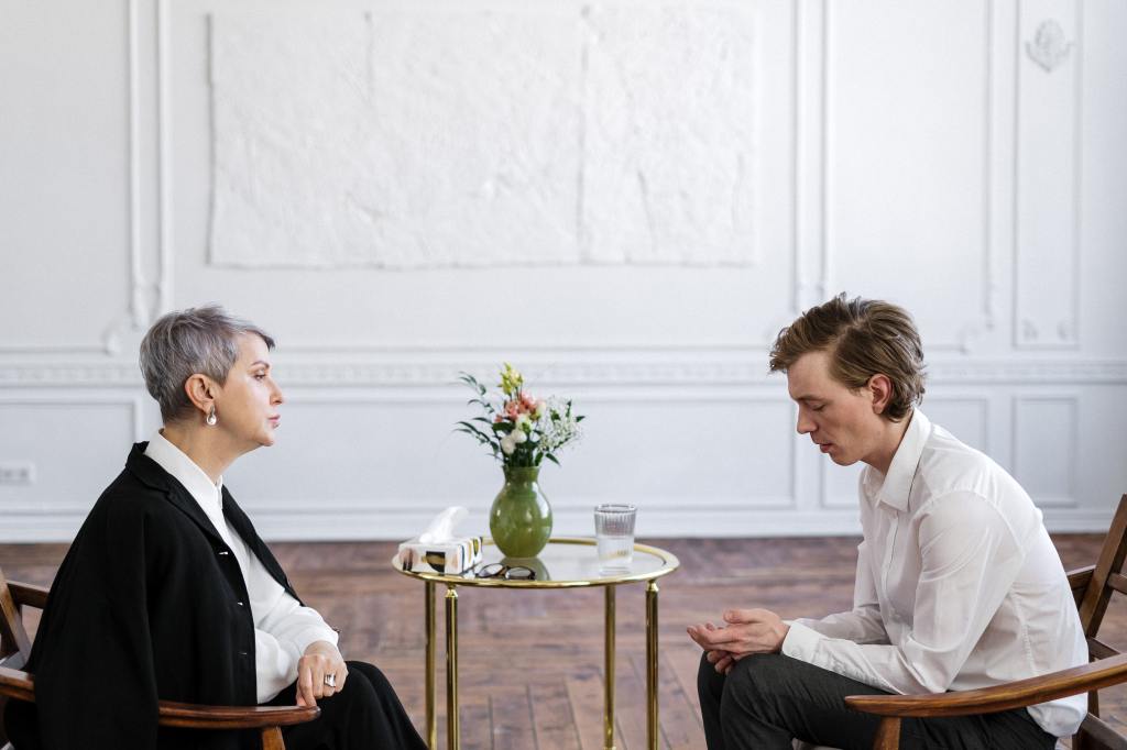 A person sitting in a comfortable chair in a therapist's office, engaged in conversation with a mental health professional, representing the act of seeking professional guidance and support for mental well-being